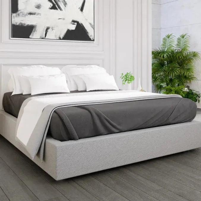 Bed with gray and white bedding in a room with plants and abstract art.